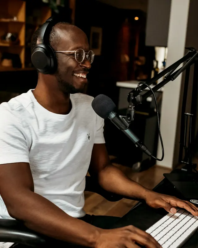 A podcast host in headphones laughing into a studio microphone
